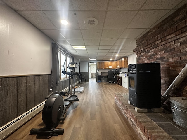 workout room featuring baseboard heating, wainscoting, a drop ceiling, and wood finished floors