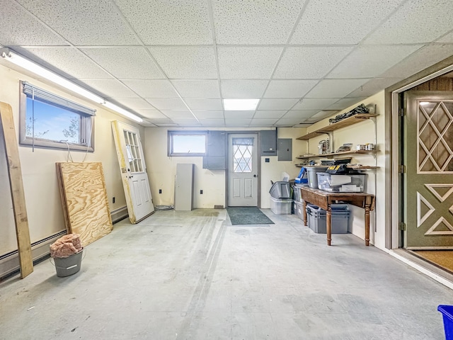 basement with a paneled ceiling, electric panel, and a baseboard heating unit