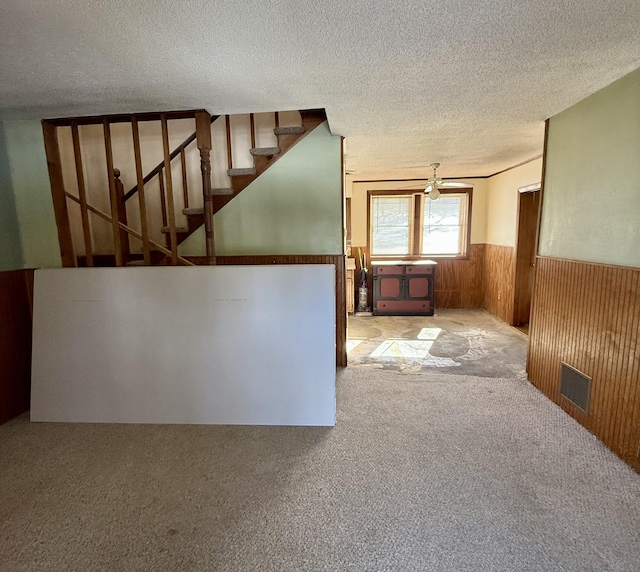 unfurnished room with a wainscoted wall, visible vents, wooden walls, a textured ceiling, and stairs