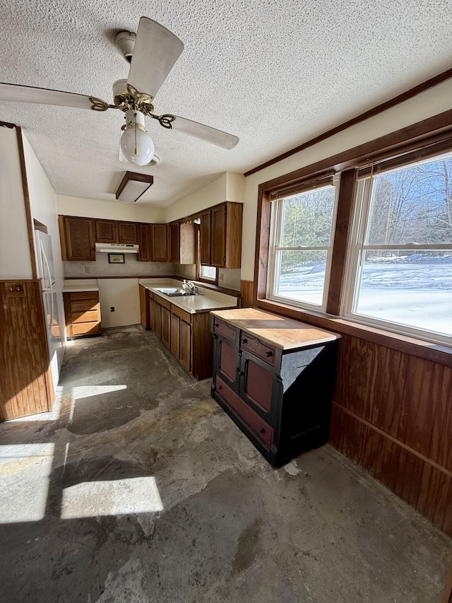 kitchen with unfinished concrete floors, light countertops, a textured ceiling, under cabinet range hood, and a sink