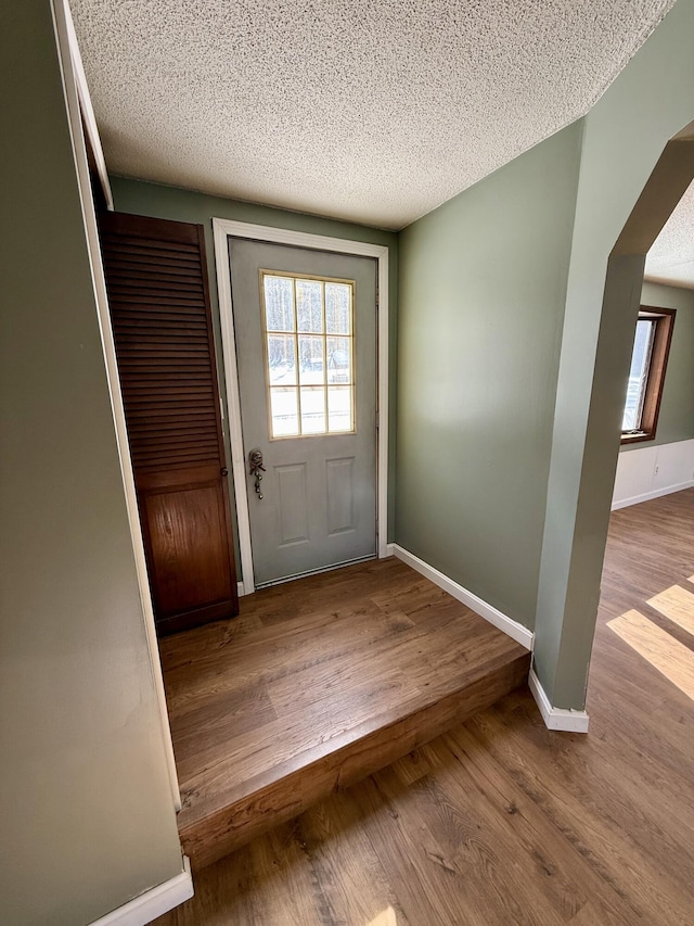 entryway with arched walkways, baseboards, light wood-style flooring, and a textured ceiling