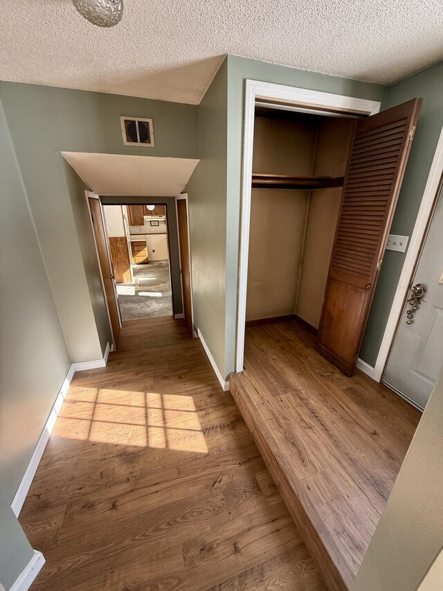 corridor featuring a textured ceiling, light wood-type flooring, visible vents, and baseboards