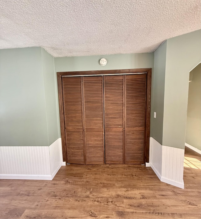 unfurnished bedroom featuring a closet, a wainscoted wall, a textured ceiling, and light wood finished floors