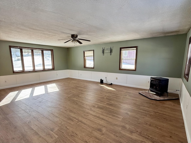 unfurnished living room featuring a wainscoted wall, dark wood-type flooring, a textured ceiling, and a wood stove