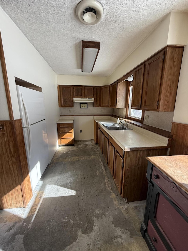 kitchen with light countertops, freestanding refrigerator, a sink, a textured ceiling, and under cabinet range hood