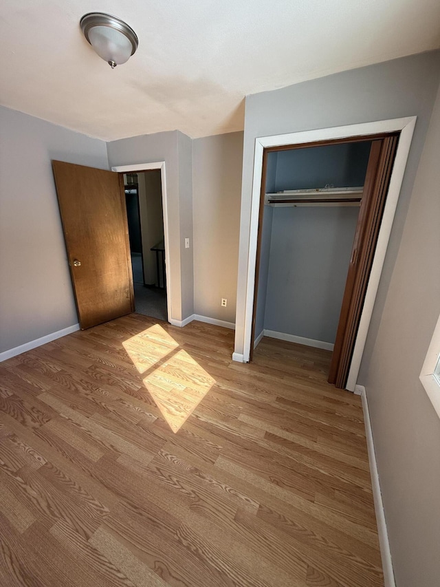 unfurnished bedroom with a closet, light wood-style flooring, and baseboards