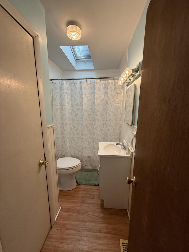 bathroom featuring toilet, a skylight, wood finished floors, visible vents, and vanity