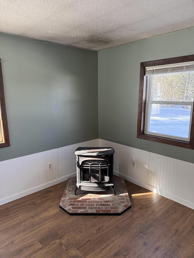 interior details with a wood stove, a wainscoted wall, a textured ceiling, and wood finished floors