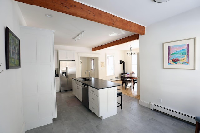 kitchen with a baseboard radiator, stainless steel appliances, white cabinetry, an island with sink, and dark countertops