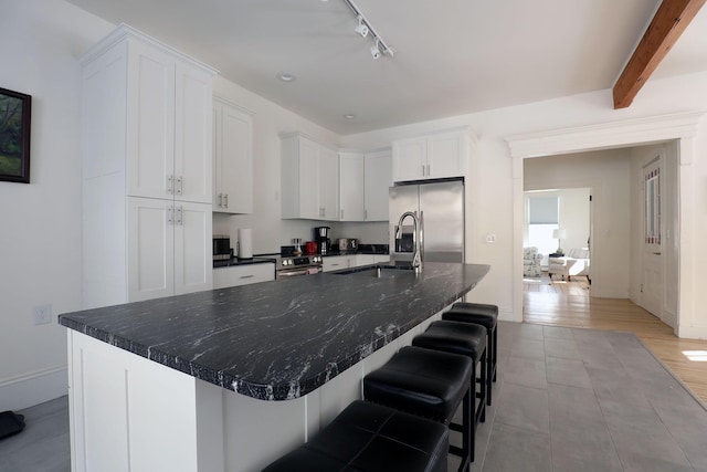 kitchen featuring a large island, a kitchen bar, stainless steel fridge, and white cabinetry