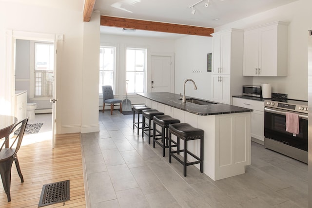 kitchen featuring a center island with sink, white cabinets, a sink, stainless steel appliances, and beam ceiling