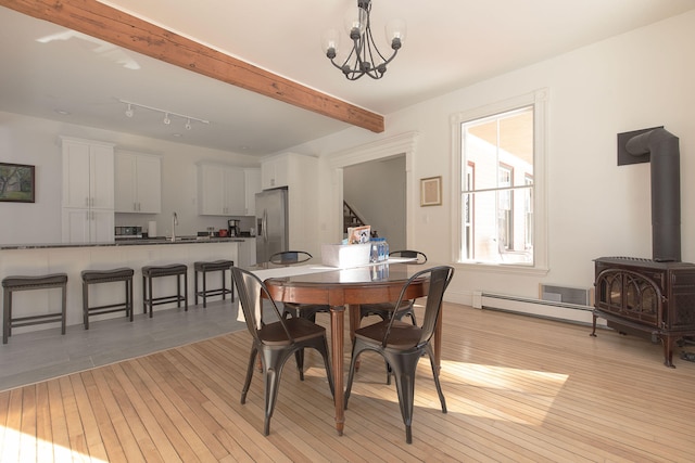 dining area featuring light wood finished floors, beamed ceiling, a wood stove, and a notable chandelier