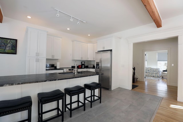 kitchen with light wood finished floors, dark stone countertops, white cabinetry, stainless steel refrigerator with ice dispenser, and a sink