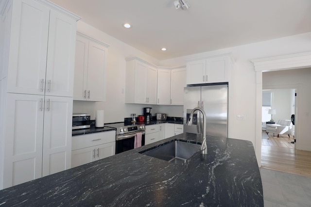 kitchen with dark stone counters, stainless steel appliances, a sink, and white cabinets