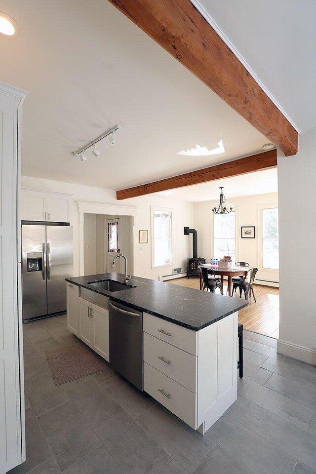 kitchen featuring white cabinets, an island with sink, appliances with stainless steel finishes, a sink, and beam ceiling