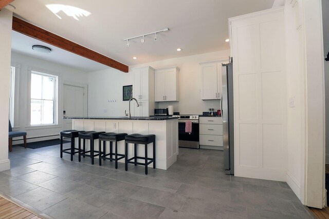 kitchen featuring a center island with sink, dark countertops, appliances with stainless steel finishes, white cabinetry, and a kitchen breakfast bar