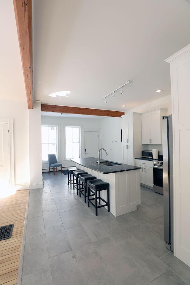 kitchen with a center island with sink, stainless steel appliances, dark countertops, white cabinets, and a sink