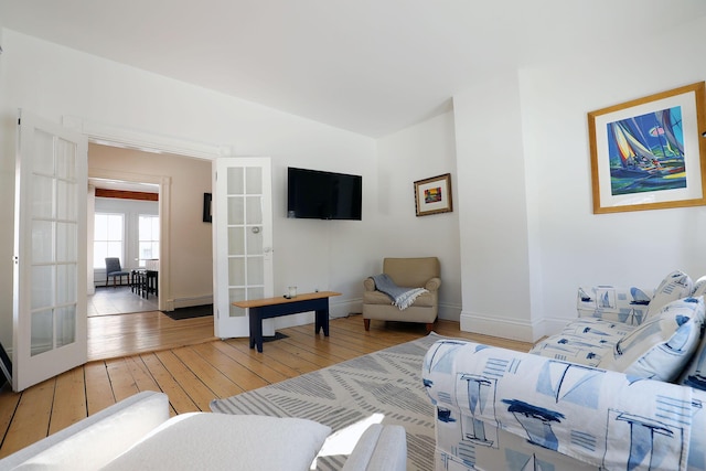 living room with baseboards, lofted ceiling, light wood-style flooring, french doors, and a baseboard heating unit