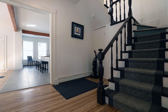 staircase featuring a baseboard heating unit, beamed ceiling, wood finished floors, and visible vents