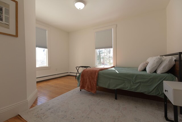 bedroom with light wood-style floors, baseboards, and a baseboard heating unit