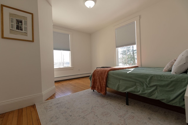 bedroom featuring light wood finished floors, baseboards, multiple windows, and a baseboard heating unit