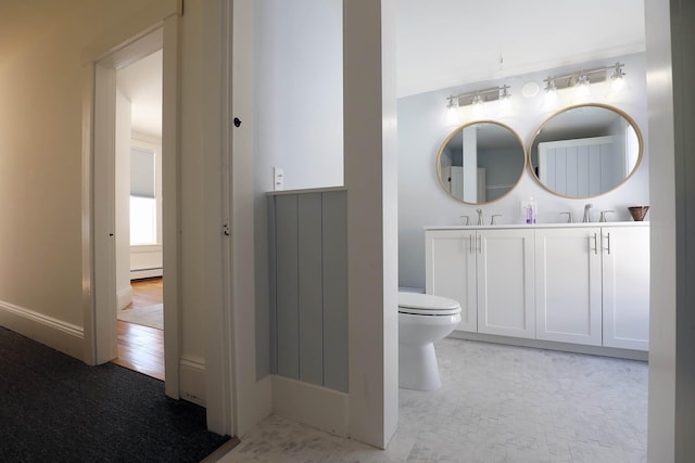 bathroom featuring a baseboard heating unit, a sink, toilet, and double vanity