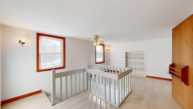 hallway with light wood-style floors, baseboards, an upstairs landing, and built in shelves