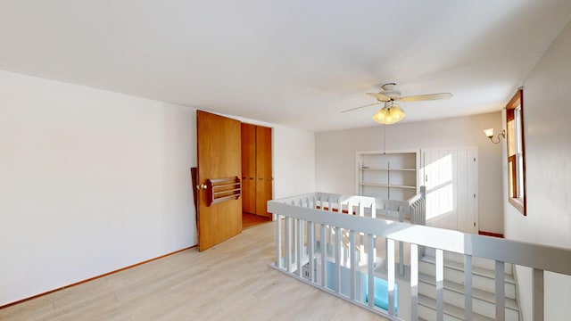 hall featuring light wood-style flooring, baseboards, and an upstairs landing