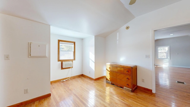 unfurnished room with visible vents, baseboards, lofted ceiling, light wood-style flooring, and a wall mounted air conditioner