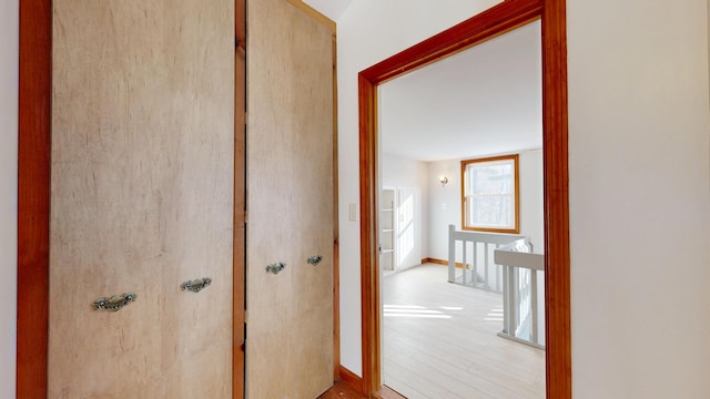 corridor featuring wood finished floors, an upstairs landing, and baseboards