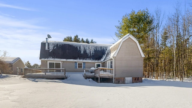 snow covered rear of property featuring a deck and a gambrel roof