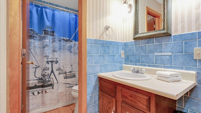 full bathroom with wallpapered walls, a shower with shower curtain, toilet, vanity, and tile walls