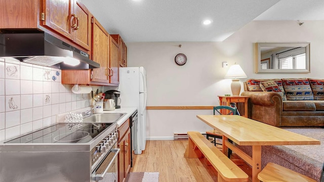 kitchen with tasteful backsplash, high end range, brown cabinetry, light wood-type flooring, and under cabinet range hood