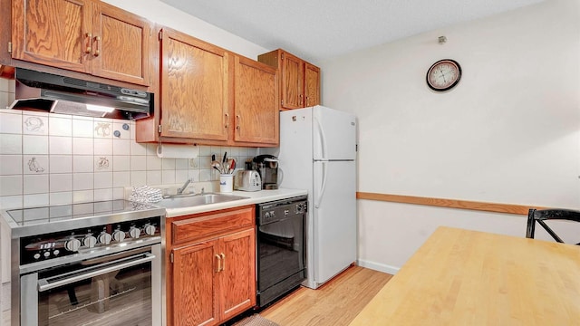 kitchen featuring under cabinet range hood, a sink, black dishwasher, stainless steel range oven, and light countertops