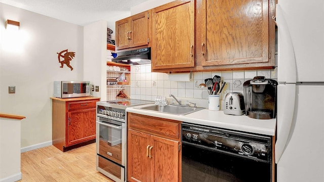 kitchen with under cabinet range hood, stainless steel appliances, light wood-style floors, light countertops, and tasteful backsplash