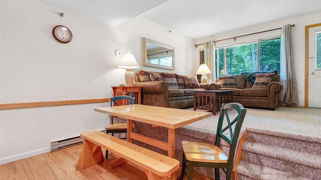 dining area with a textured ceiling, a baseboard heating unit, light wood finished floors, and baseboards