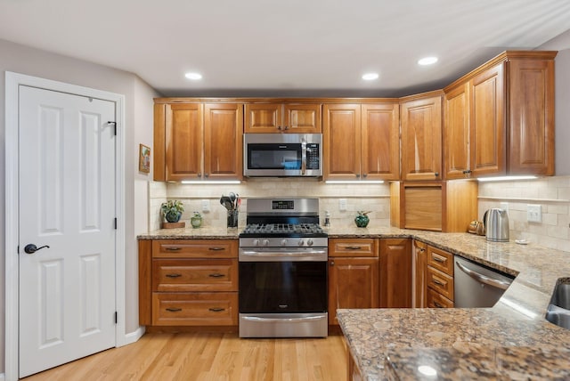 kitchen with light stone counters, stainless steel appliances, light wood-style floors, backsplash, and brown cabinetry