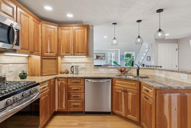 kitchen featuring light wood finished floors, light stone counters, a peninsula, stainless steel appliances, and a sink