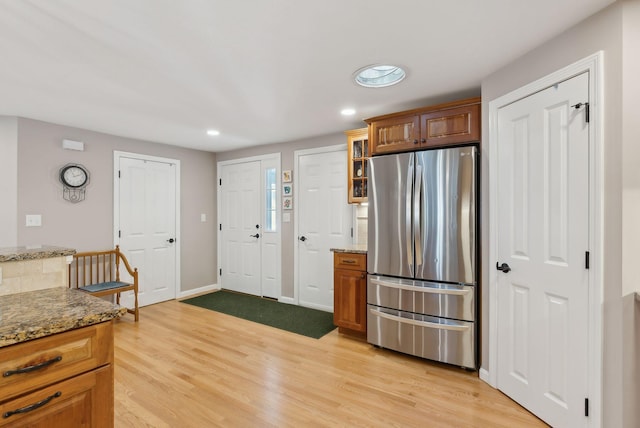 kitchen with light stone counters, glass insert cabinets, freestanding refrigerator, light wood-type flooring, and recessed lighting