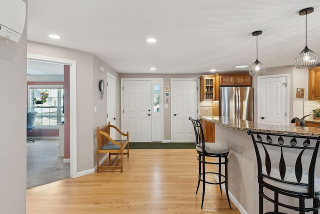 kitchen featuring light wood finished floors, brown cabinetry, a breakfast bar, decorative light fixtures, and freestanding refrigerator