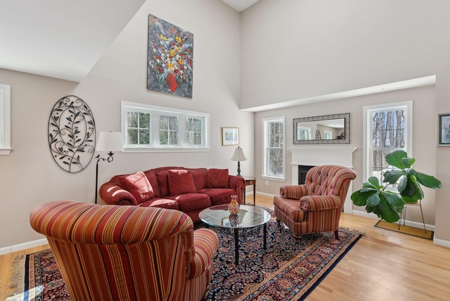 living room with a towering ceiling, a fireplace, baseboards, and wood finished floors