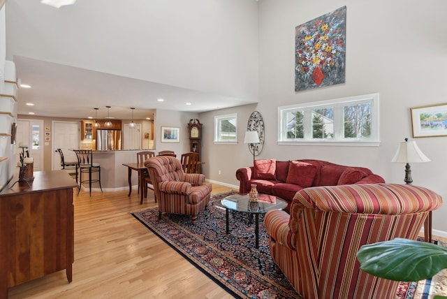 living area with light wood-style flooring, a high ceiling, baseboards, and recessed lighting