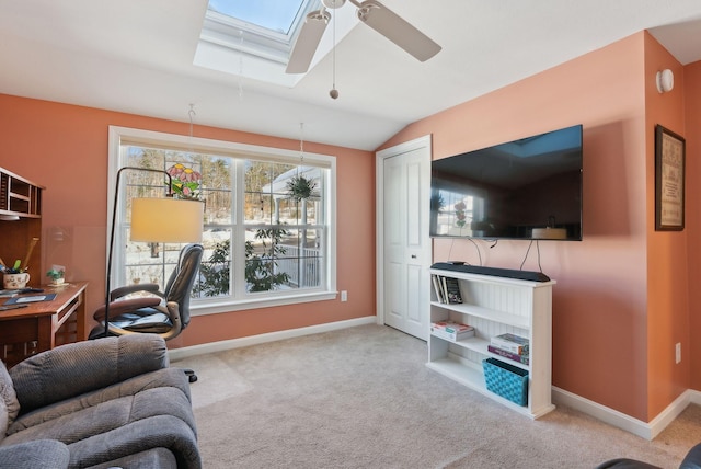 carpeted office featuring vaulted ceiling with skylight, a ceiling fan, and baseboards