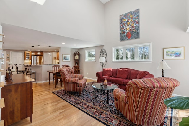 living room with a towering ceiling, light wood-style floors, baseboards, and recessed lighting