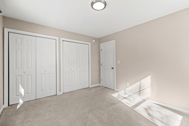 unfurnished bedroom with light carpet, baseboards, and multiple closets