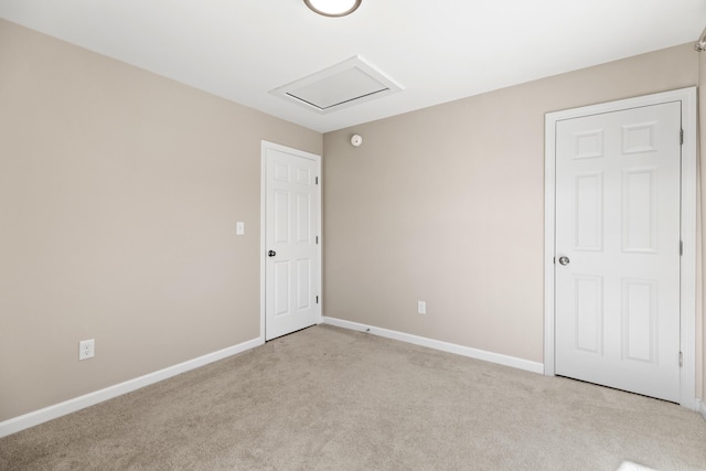 empty room featuring light carpet, attic access, and baseboards