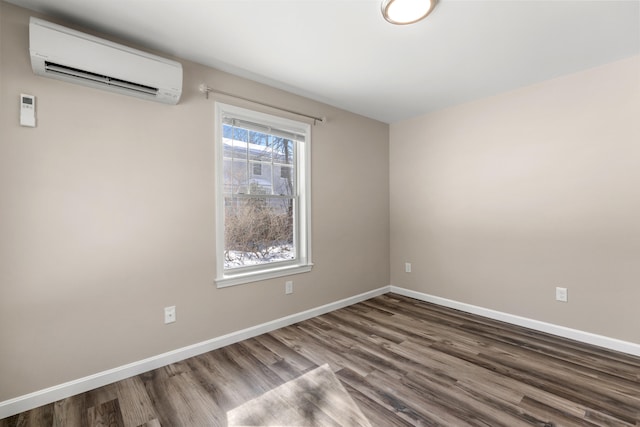 spare room featuring a wall unit AC, baseboards, and wood finished floors