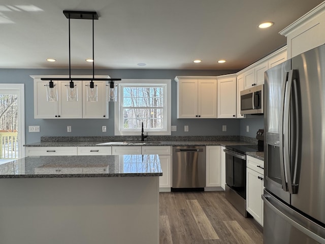 kitchen with decorative light fixtures, appliances with stainless steel finishes, white cabinets, a sink, and dark stone countertops