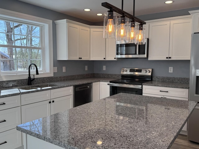 kitchen with appliances with stainless steel finishes, a center island, white cabinetry, and a sink