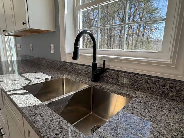 room details featuring stone counters, white cabinets, and a sink